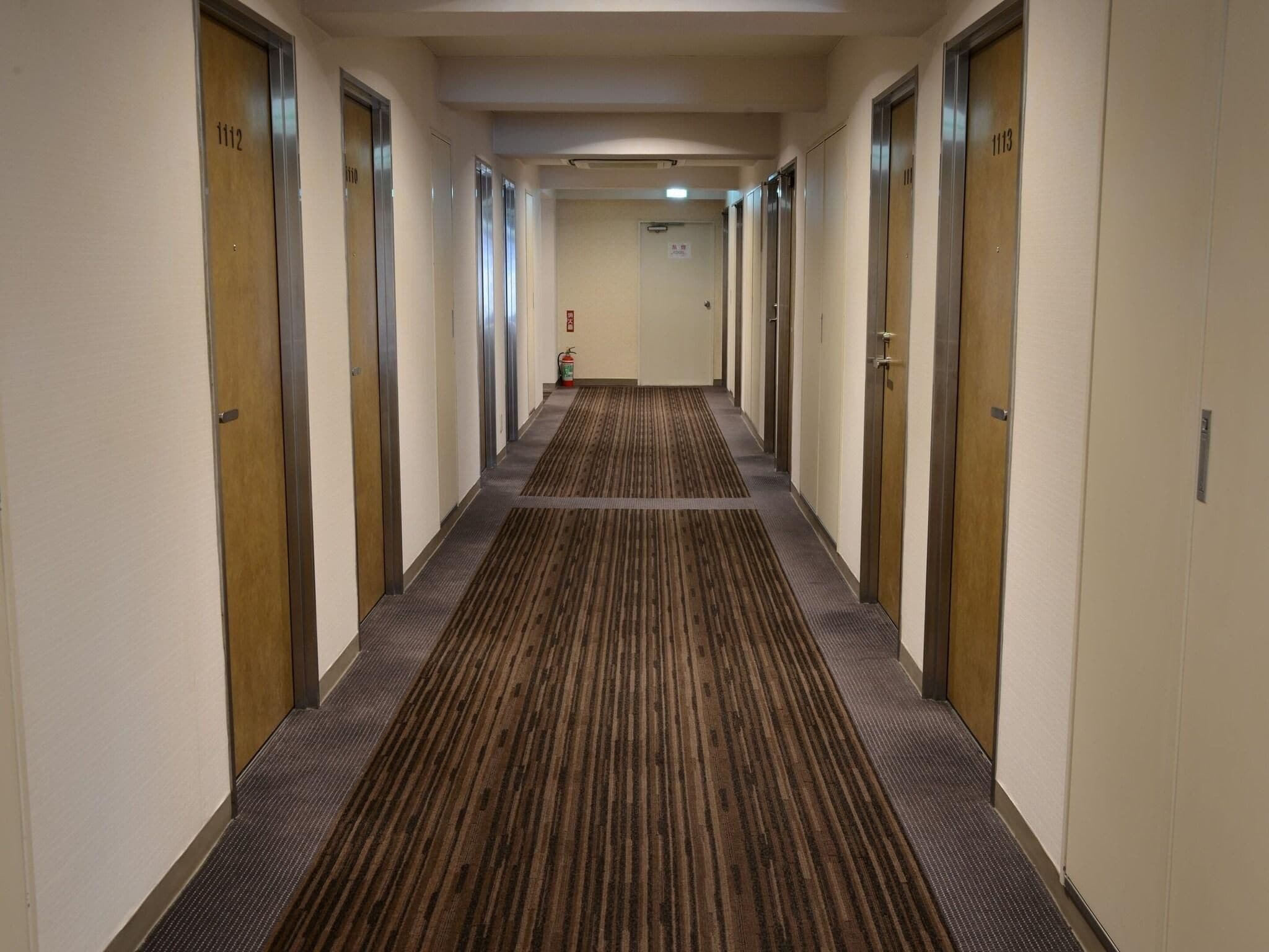 Ein Hotelkorridor mit Teppichböden, Türen mit den Nummern 1112 und 1113 sowie einem Feuerlöscher an der Wand.