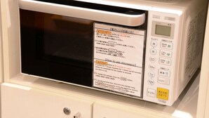 Un horno microondas con pantalla digital y panel de control, ubicado en un estante sobre un gabinete blanco.