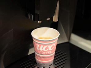 Une machine à café qui verse le café dans un gobelet en papier portant le logo de la marque.