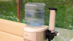Dispensador de agua con una botella de agua Aqua Clara, un dispensador y un panel de control con un letrero de advertencia.