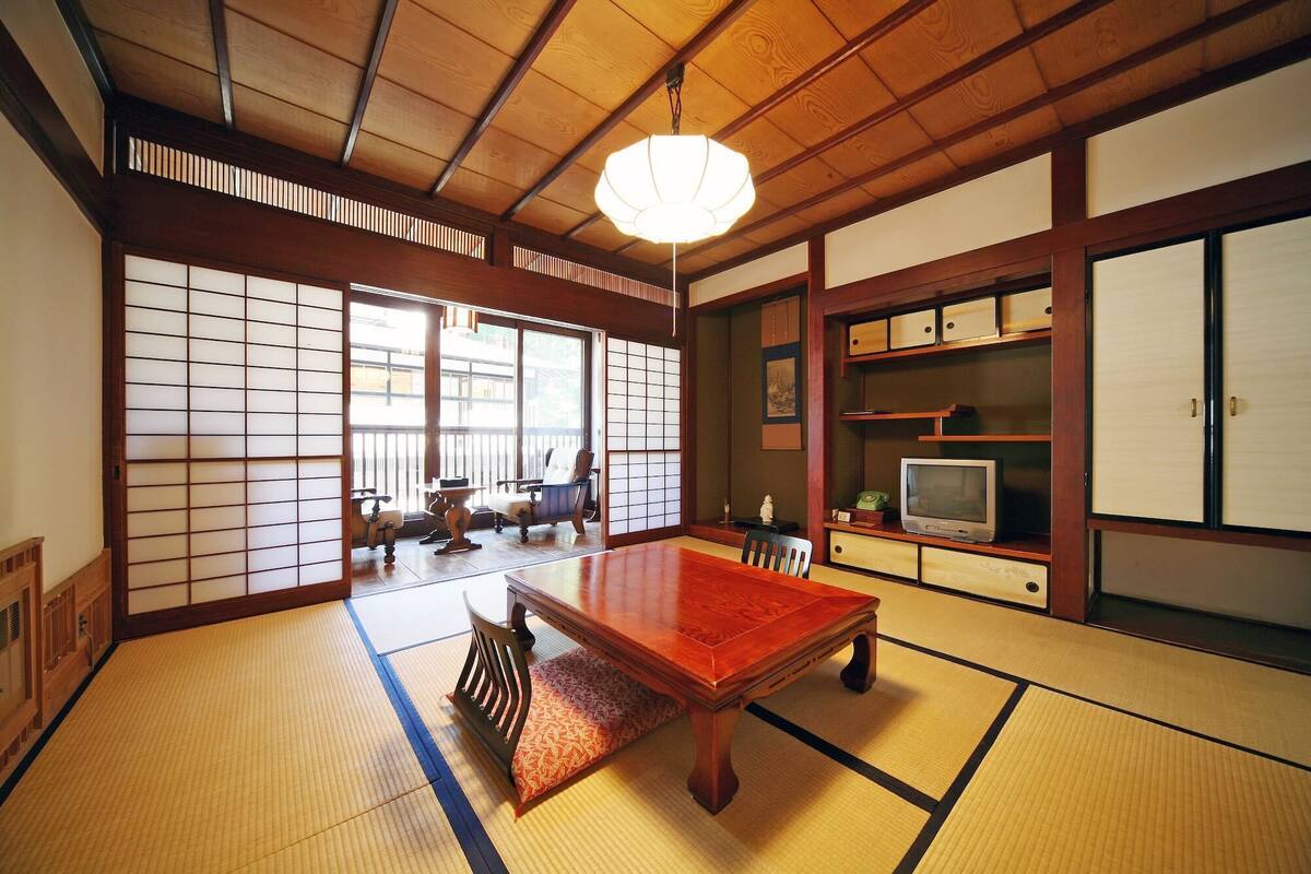 A traditional Japanese room with tatami flooring, a wooden table, a television, and sliding doors.