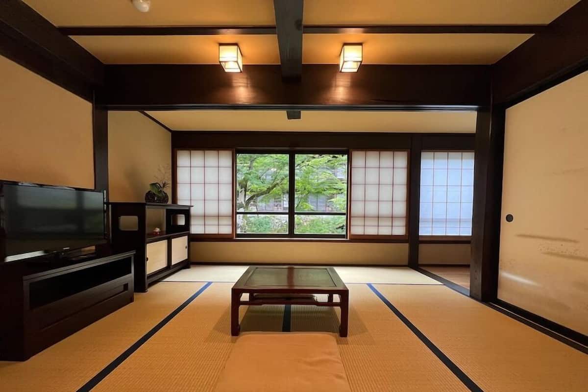Una habitación tradicional japonesa con suelo de tatami, televisor, una mesa baja y puertas correderas.