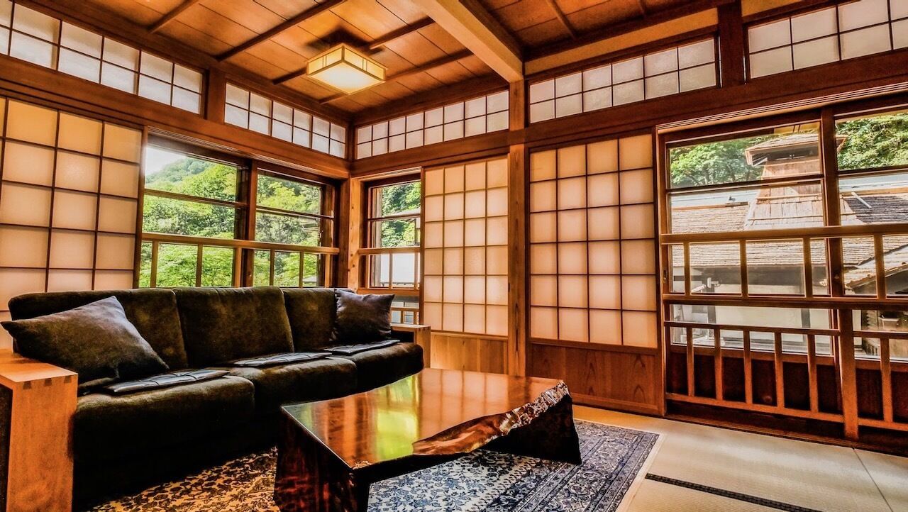 Una habitación japonesa tradicional con suelo de tatami, una mesa de madera baja, un sofá y amplios paneles de shoji.
