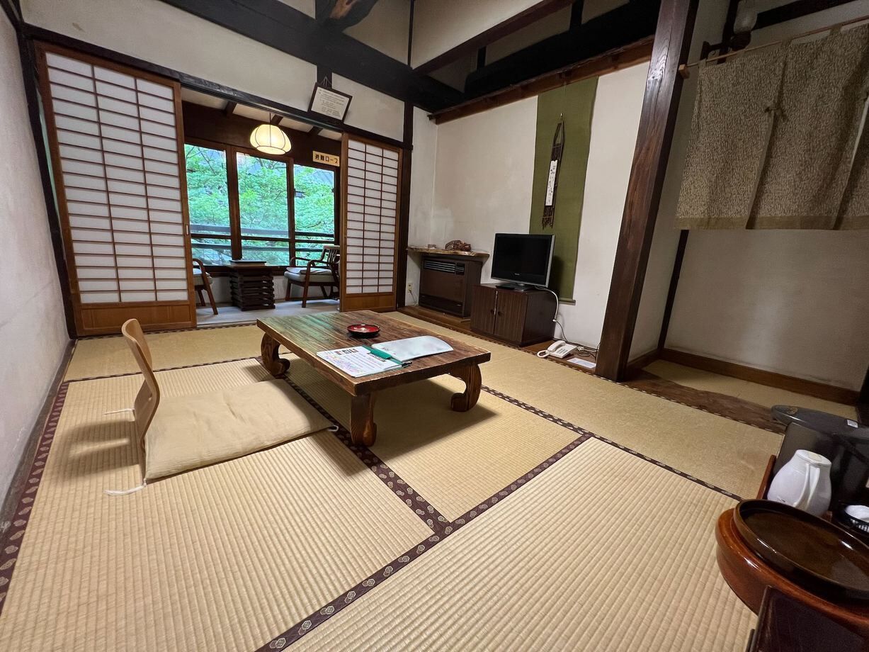 Une pièce de style japonais traditionnel, avec un sol recouvert de tatamis, une petite table en bois, un téléviseur et une porte coulissante donnant sur un balcon.