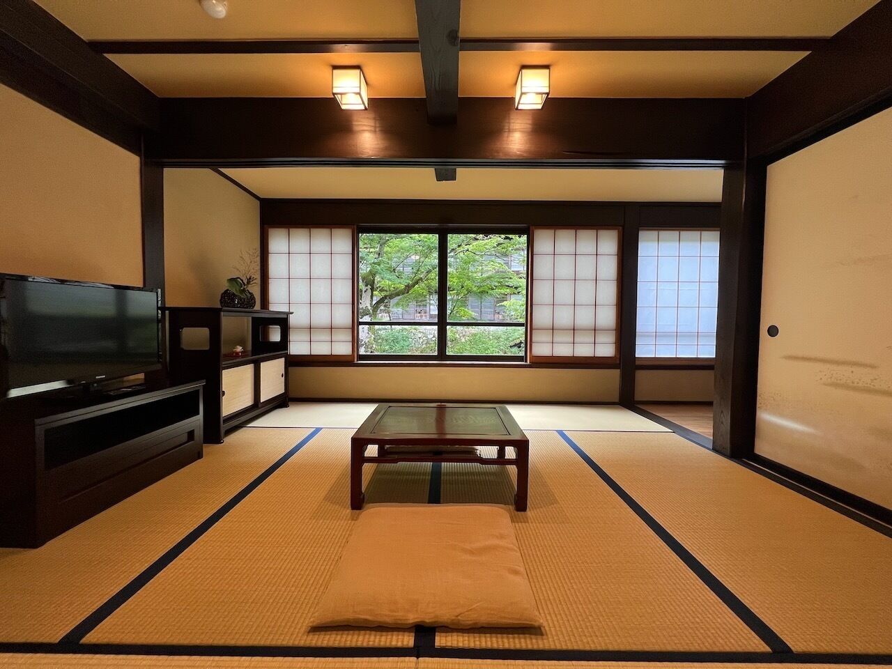 Una habitación japonesa tradicional con suelo de tatami, una mesa baja, un televisor y puertas correderas.