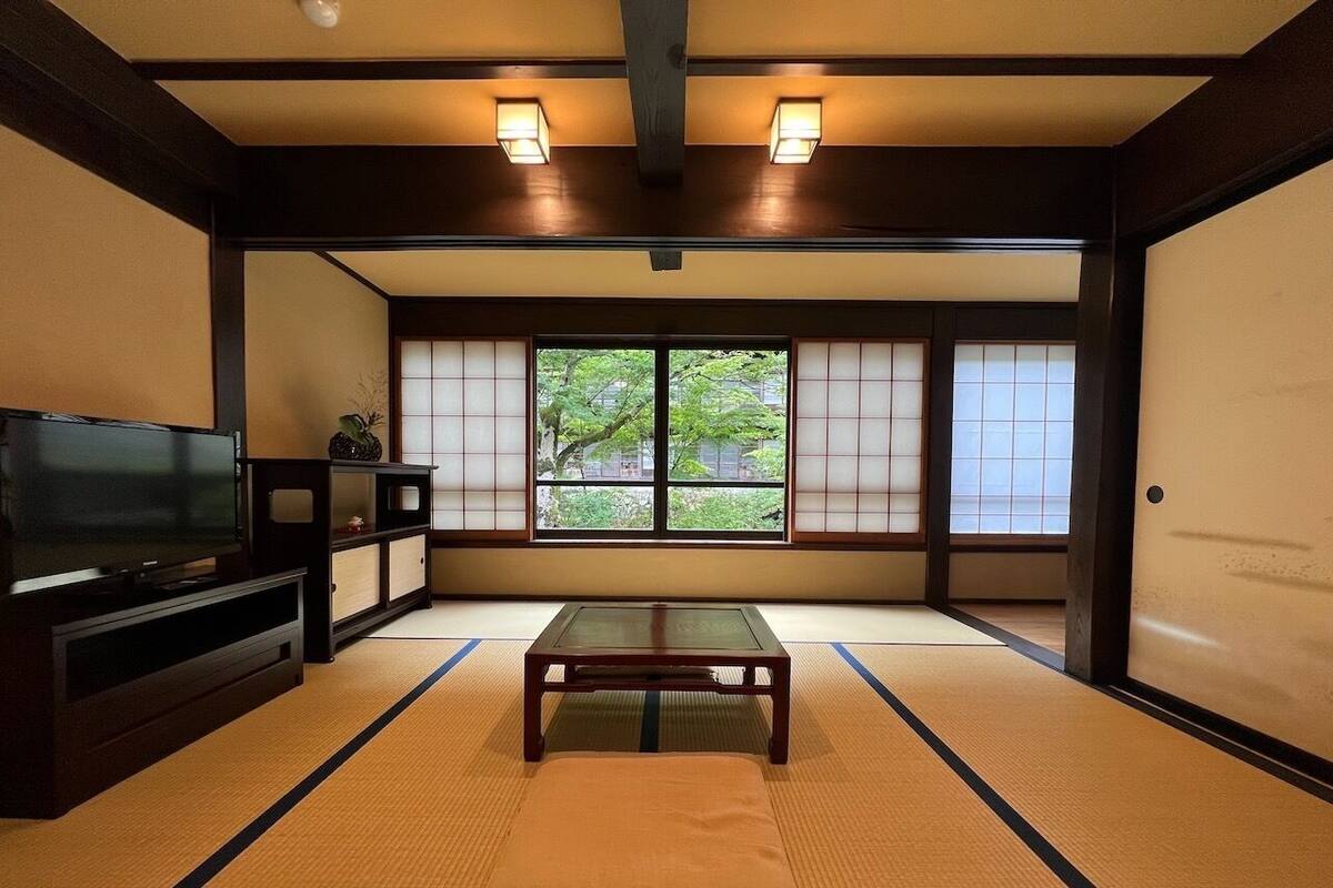 A traditional Japanese room with tatami flooring, a low table, a TV, and sliding doors.
