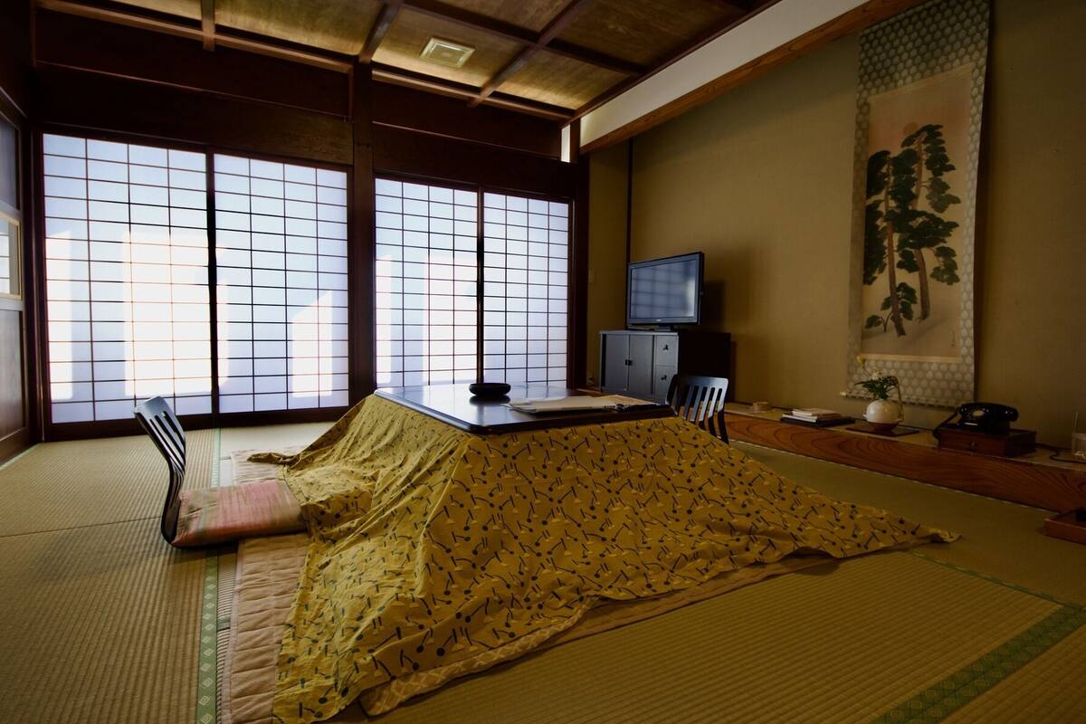 A tatami mat room with a low table, a chair, a television, and a traditional Japanese painting.