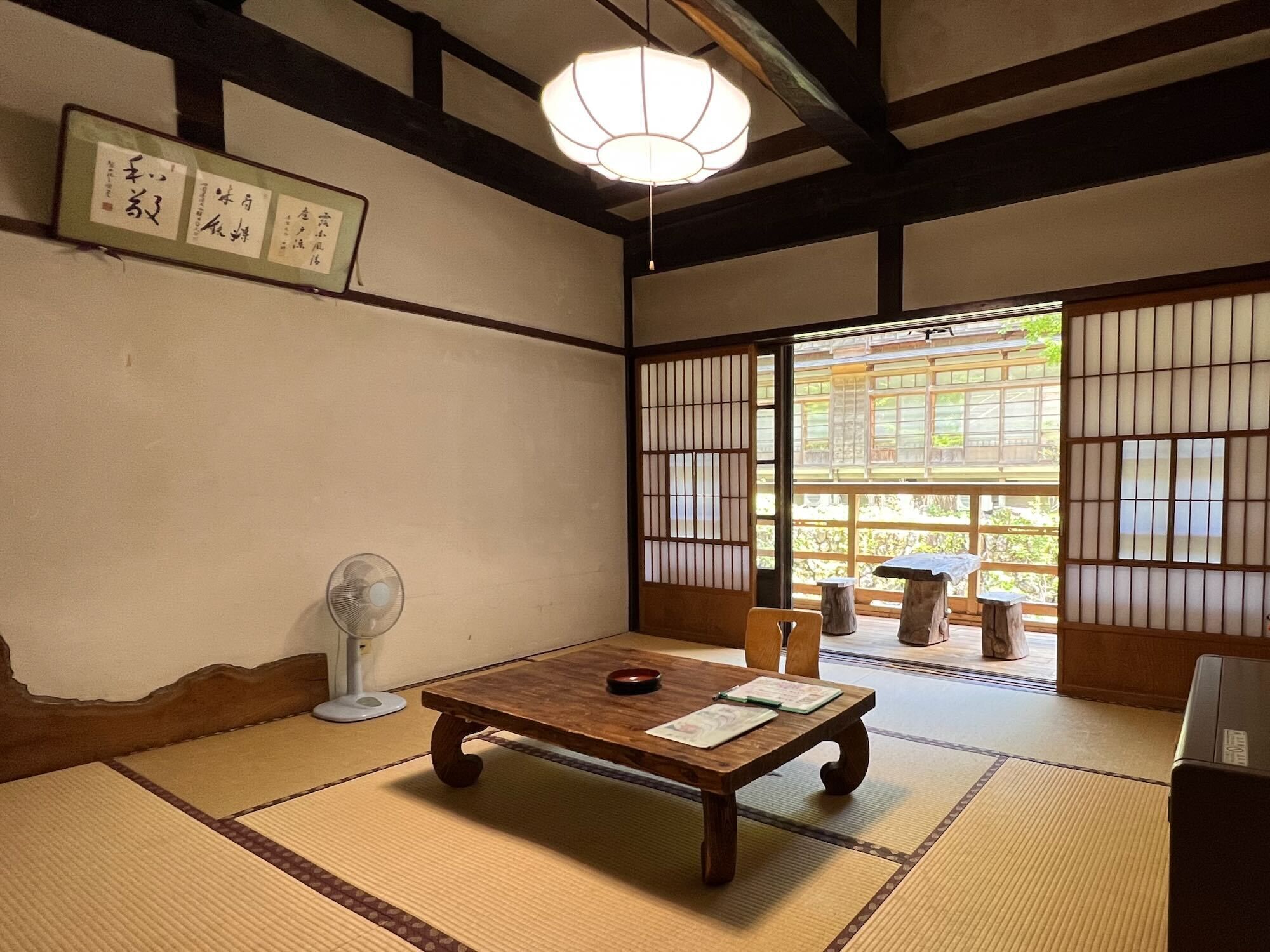 Une pièce de style japonais traditionnel, avec un sol recouvert de tatamis, une petite table en bois, un éventail et des paravents en papier.