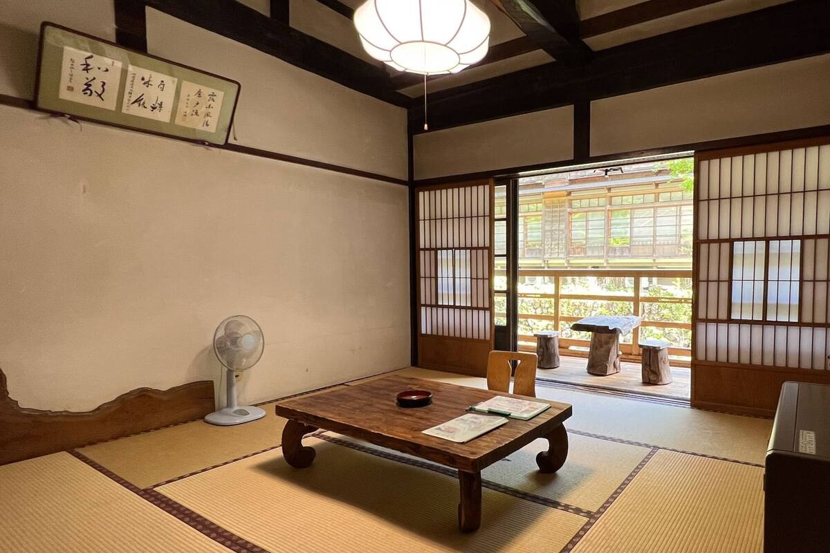 A traditional Japanese room with tatami flooring, a low wooden table, a fan, and shoji screens.