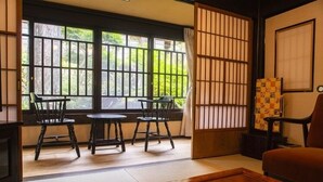 Ein traditioneller japanischer Raum mit Tatami-Bodenbelag, einem niedrigen Tisch, zwei Stühlen und einer Schiebetür.