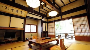 Una habitación japonesa tradicional con suelo de tatami, una mesa de madera baja, puertas correderas y un televisor.