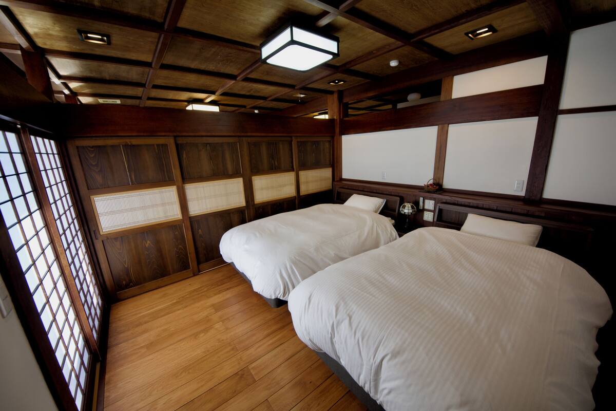 A traditional Japanese-style room with two beds, wooden flooring, tatami mats, and shoji screens.