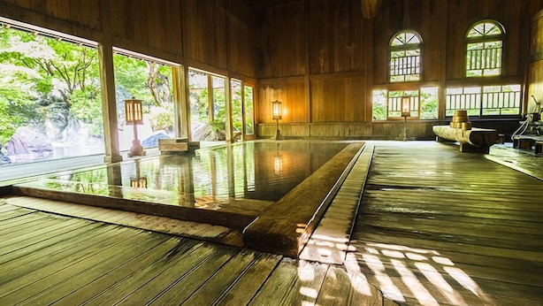 Un balneario de madera tradicional con una amplia piscina interior, suelo de madera y grandes ventanales que dejan entrar luz natural.