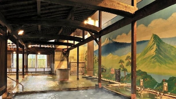 Ein traditionelles japanisches Onsen mit einem großen Thermalbad, Holzbalken und einer Wandmalerei einer Berglandschaft.
