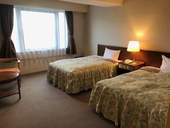 A hotel room with two beds, a desk, a chair, and a window with curtains. - Sky Hotel (Matsuyama)