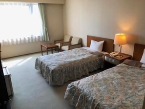A hotel room with two beds, a desk, a chair, and a lamp. - Sky Hotel (Matsuyama)