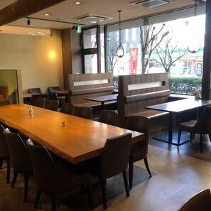 A restaurant interior with a long wooden table, several booths, and chairs. - Sky Hotel (Matsuyama)