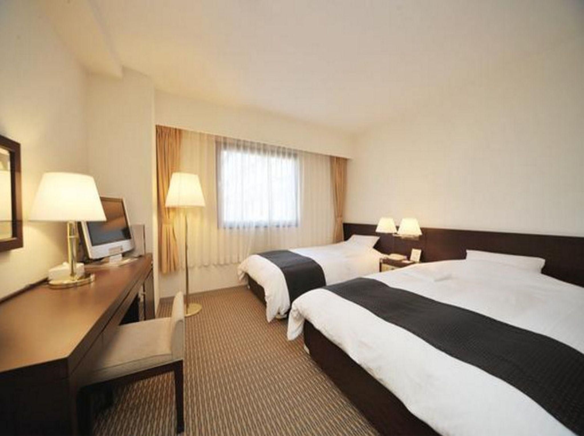 A hotel room with two beds, a desk with a computer, and a lamp.