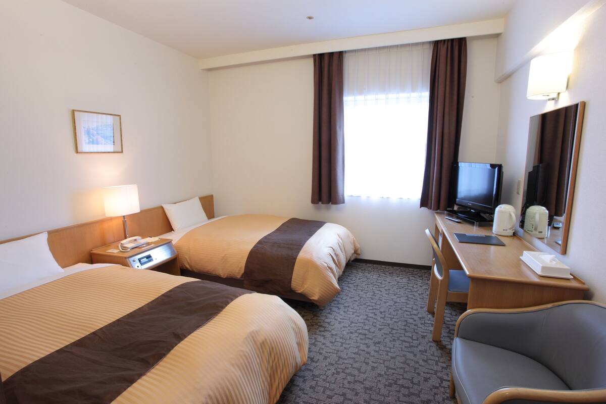 A hotel room with two beds, a desk with a computer, a chair, and a television.