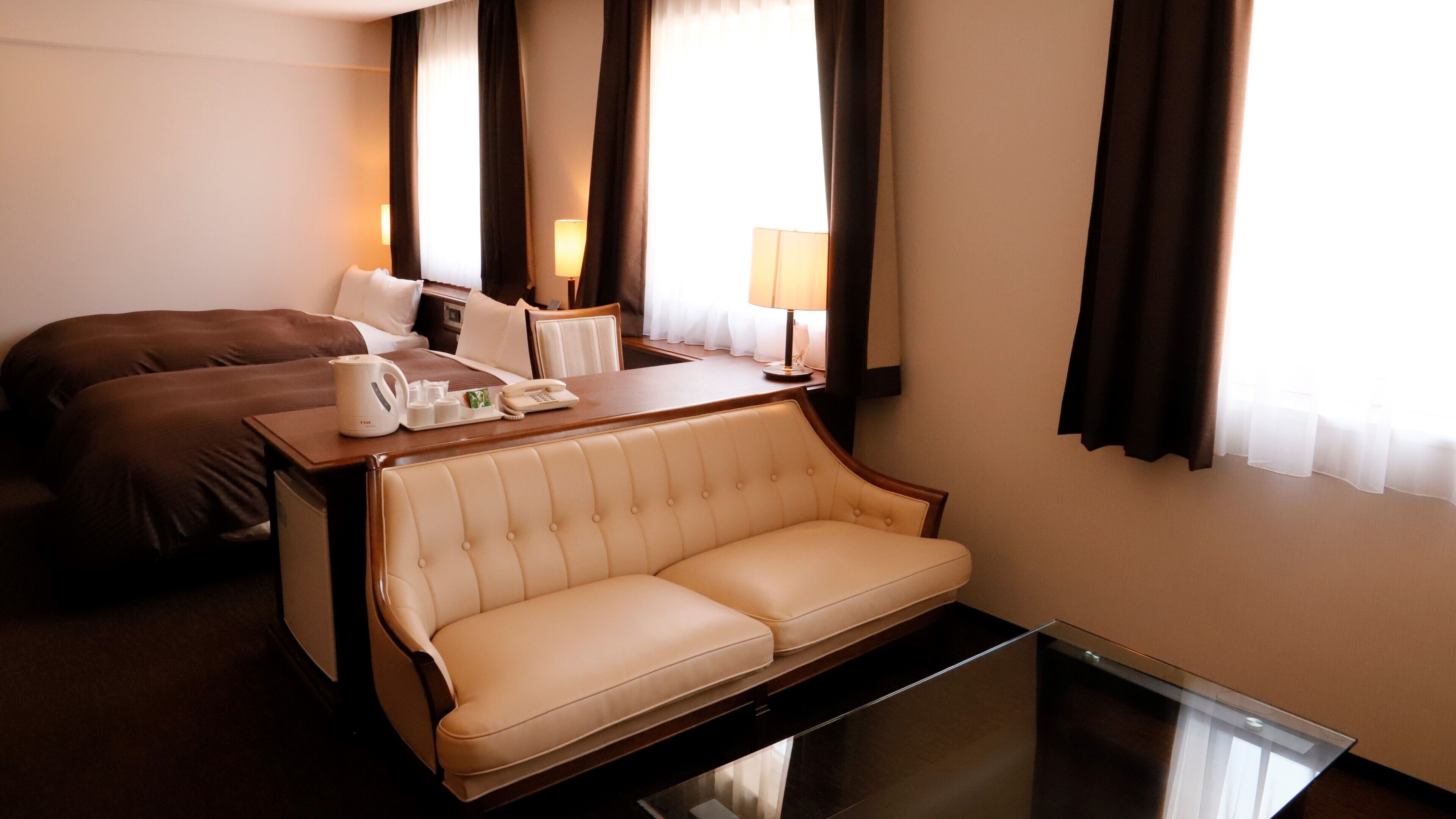 A hotel room with a bed, a sofa, a desk with a telephone, a coffee maker, and a lamp.