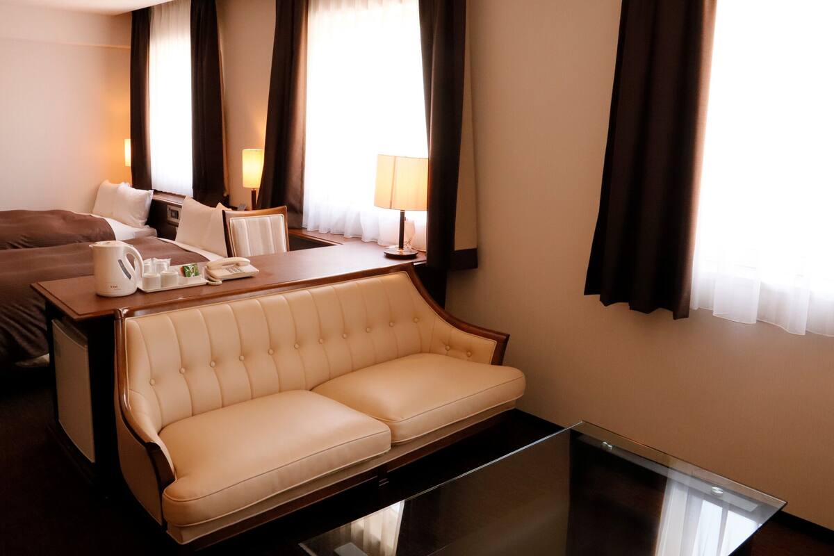 A hotel room with a bed, a sofa, a desk with a telephone, a coffee maker, and a lamp.