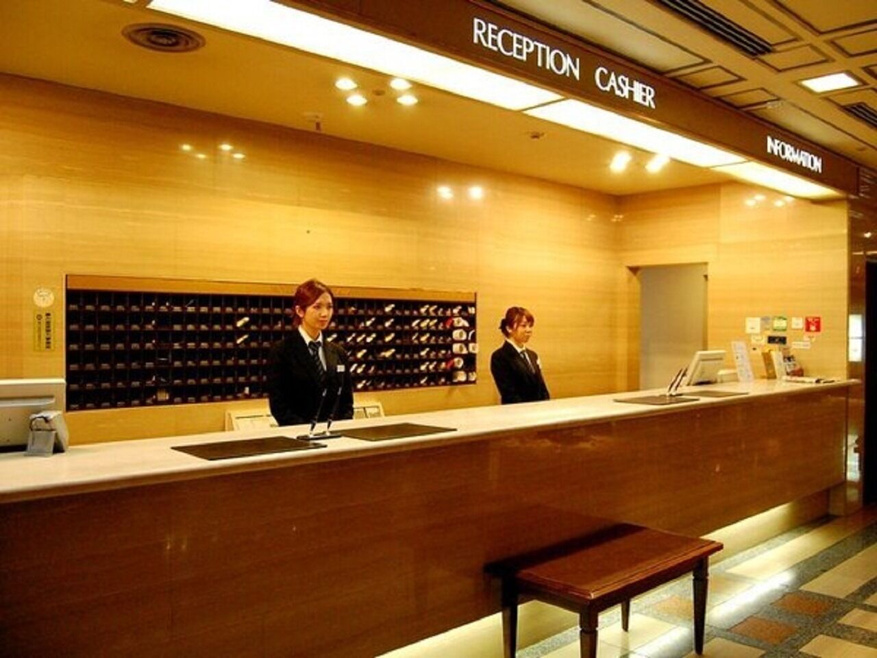 Zona de recepción con mostrador, dos empleados y una exhibición de zapatos.