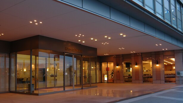 A modern hotel entrance with glass doors, a sign reading "Hotel Green Park," and a tiled walkway leading to the entrance.