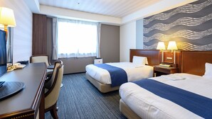 A hotel room with two beds, a desk, a chair, a telephone, and a large abstract wall mural.
