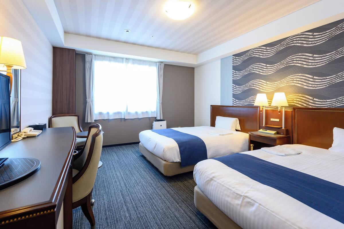 Een hotelkamer met twee bedden, een bureau, een stoel, een telefoon en een groot abstracte muurschildering.