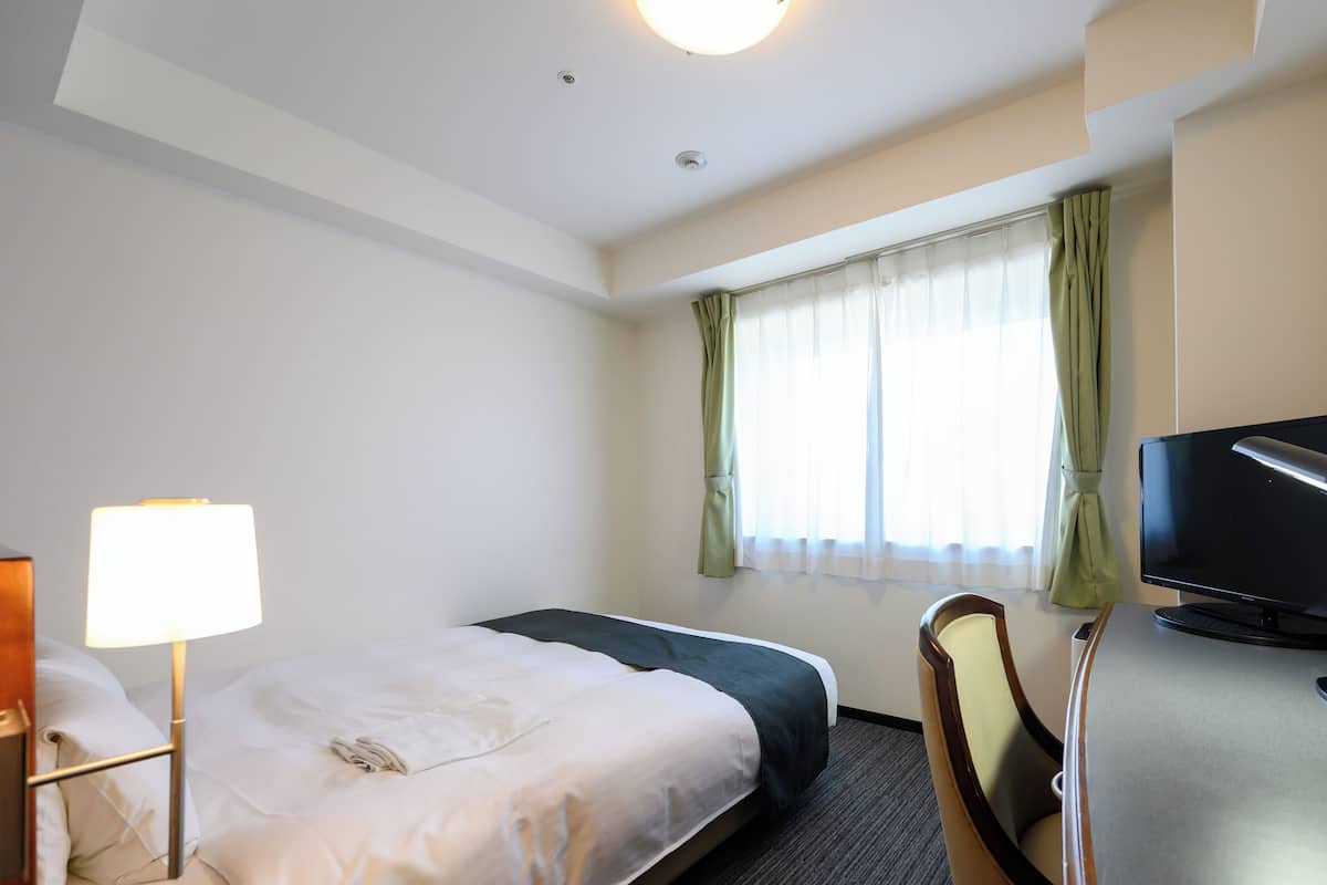 Een hotelkamer met een bed, een bureau met stoel, een televisie en een lamp.