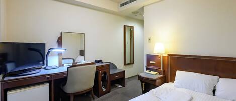 Habitación de hotel con cama, escritorio con computadora, silla, televisor y lámpara.