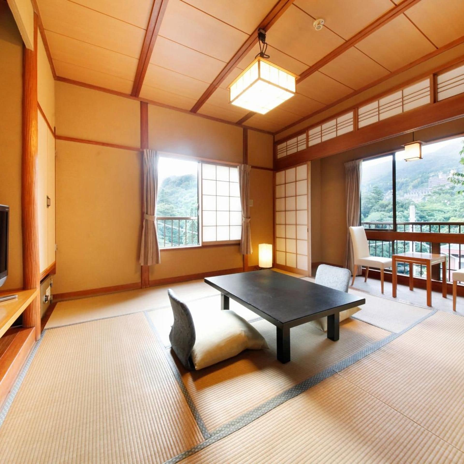Une pièce de style japonais traditionnel, avec un sol recouvert de tatamis, une table basse, un canapé et une vue sur un paysage montagneux.