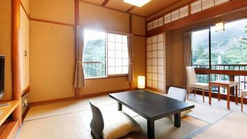 Une pièce de style japonais traditionnel, avec un sol recouvert de tatamis, une table basse, un canapé et une vue sur un paysage montagneux.
