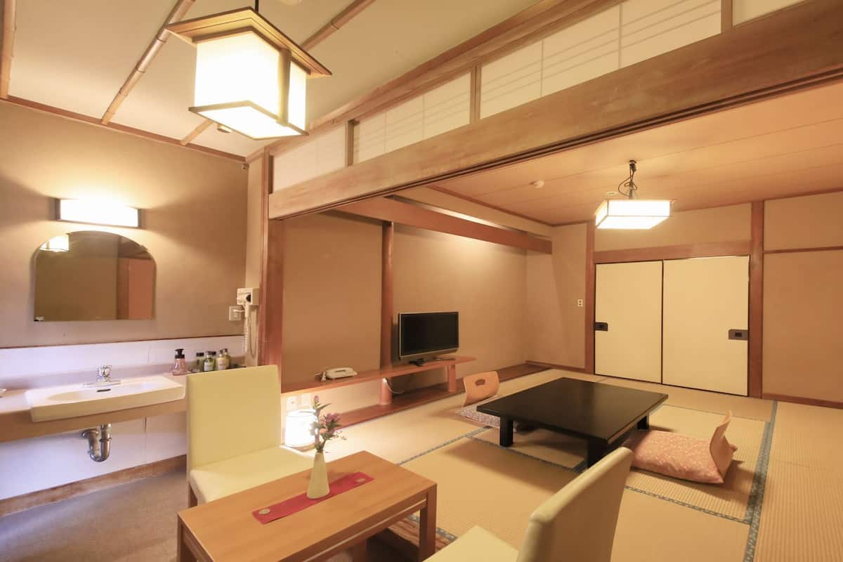A traditional Japanese-style room with tatami flooring, a television, a desk, and a sofa.