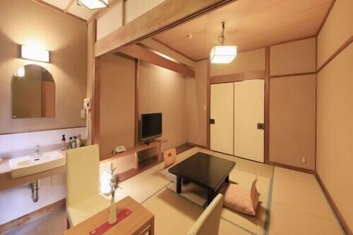 A traditional Japanese-style room with tatami flooring, a low table, a television, and sliding doors.
