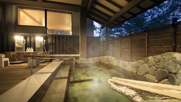 Un área de baño con aguas termales, paredes de piedra y una terraza de madera.