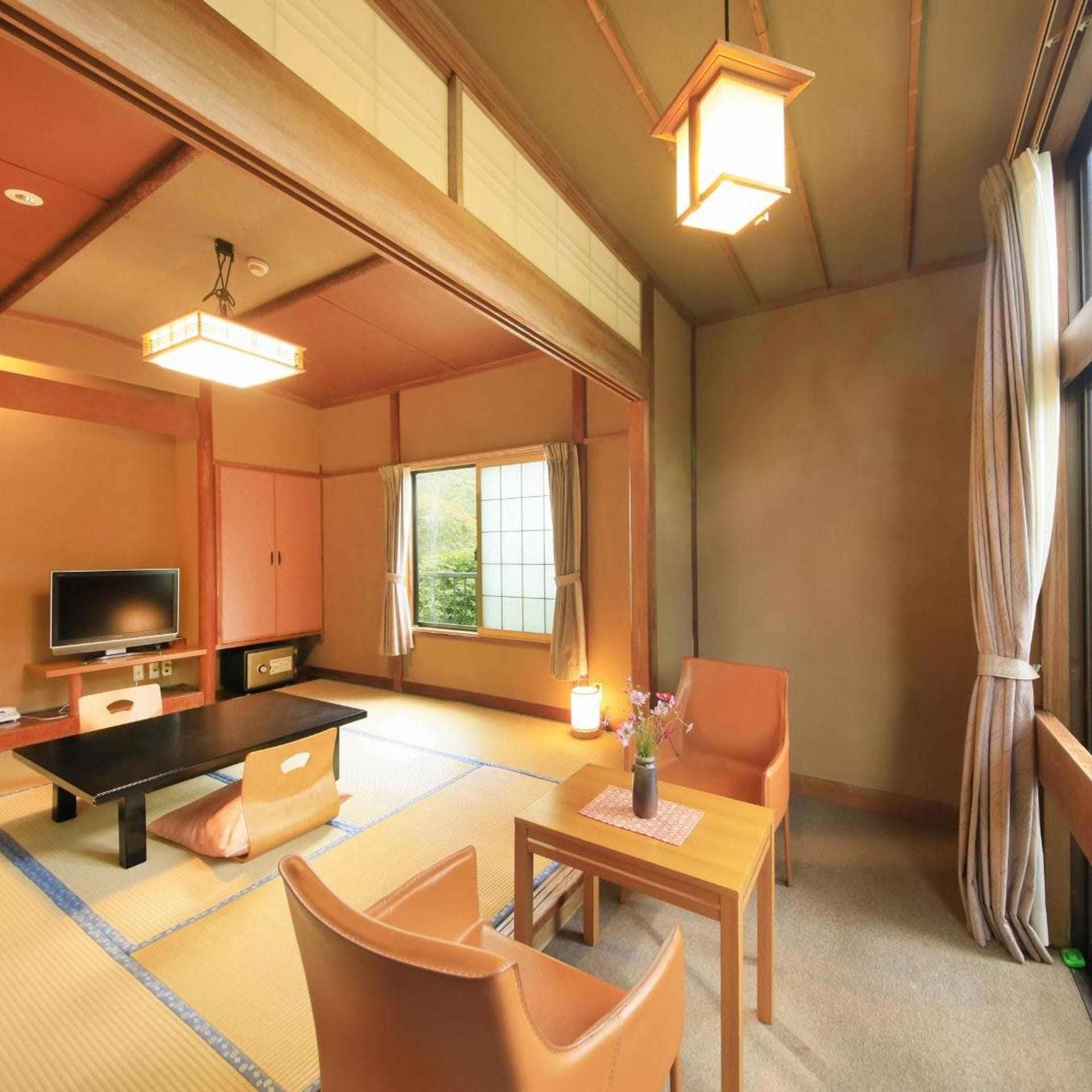 A traditional Japanese room with tatami flooring, a low table with a vase, a television, and a sofa.