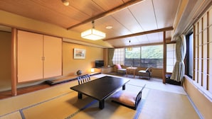 A traditional Japanese room with tatami flooring, a low table, a television, and a view of greenery outside. - Yugawara Ohnoya Ryokan (Atami)