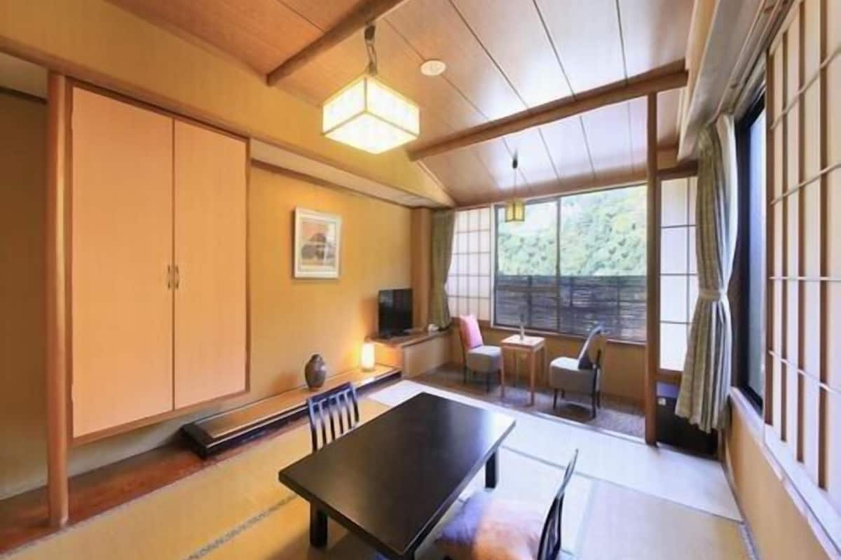 A traditional Japanese room with tatami flooring, a low table, sliding doors, and a view through a large window.