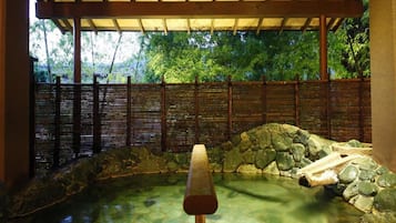 Um jardim japonês tradicional com lago de pedra, cerca de madeira e um caminho de madeira.