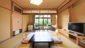 Una habitación de estilo japonés tradicional con suelo de tatami, una mesa baja, un televisor y vistas al exterior.