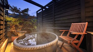 Un jacuzzi con una silla de madera, rodeado por una terraza de madera y una cerca de madera.