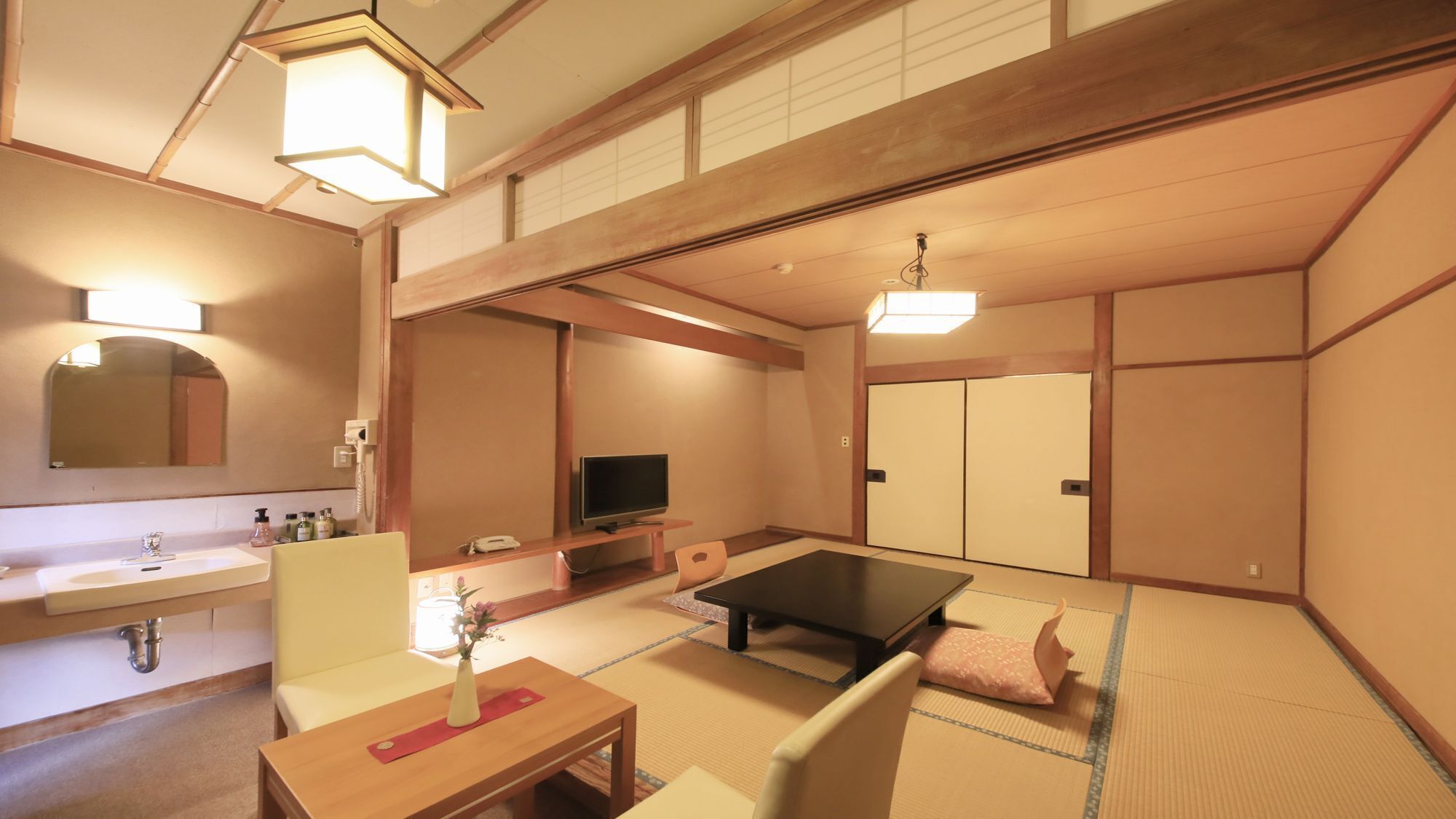 A traditional Japanese room with tatami flooring, a television, a desk, and a sofa.
