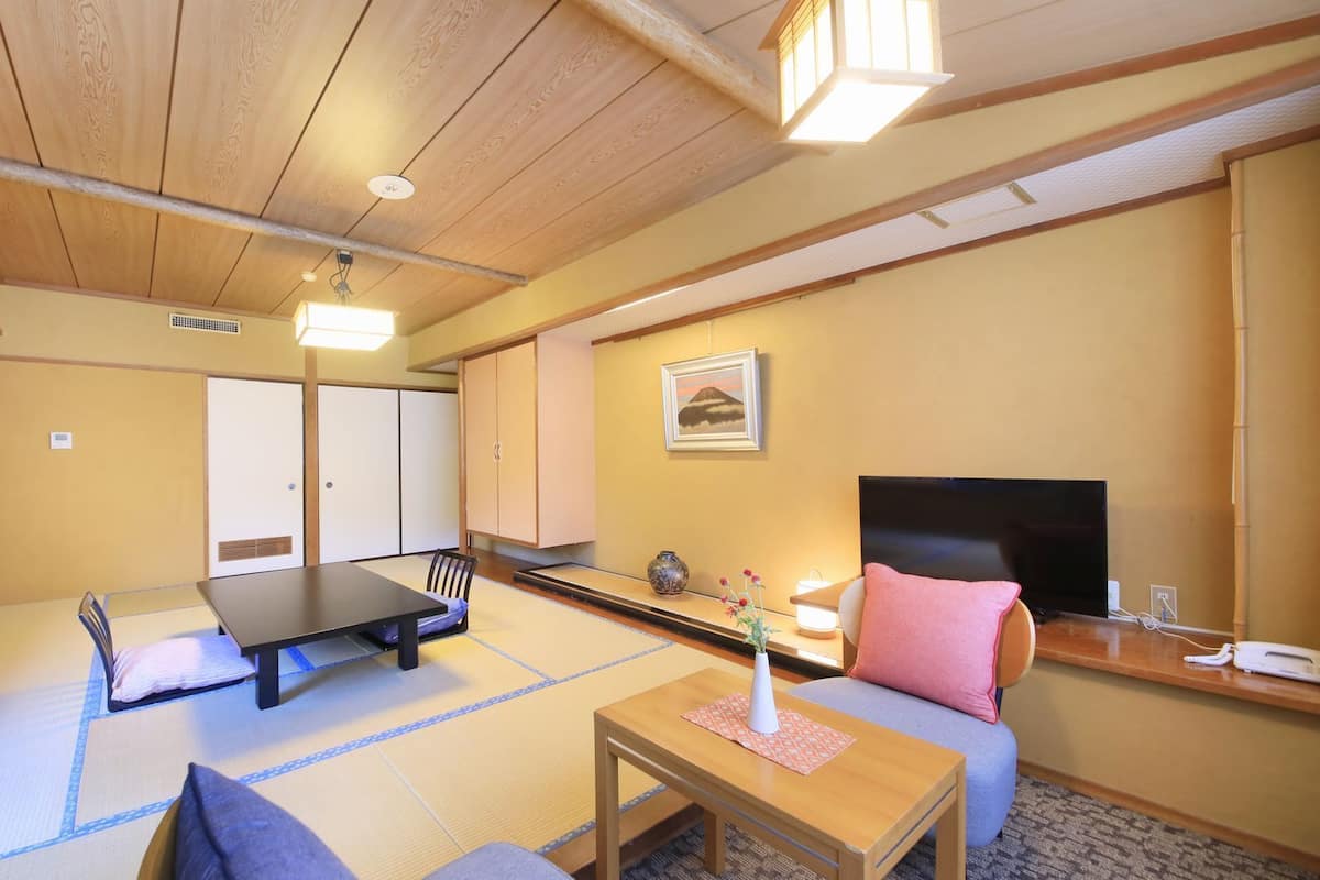 A traditional Japanese room with tatami flooring, a low table, a sofa, and a television.