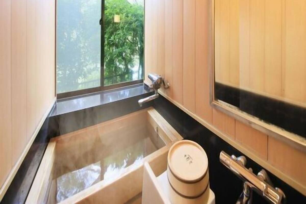 A bathroom with a bathtub, a window, and wooden paneling.