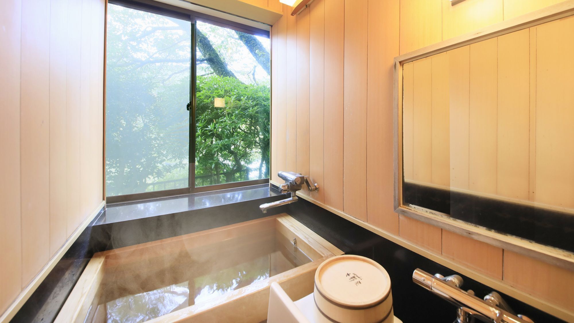 A traditional Japanese-style bathroom with a large soaking tub, a wooden sliding door, and a view of greenery outside.