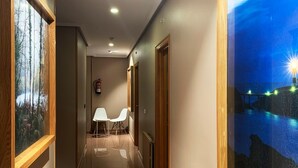 Ein Hotelkorridor mit einem Holzbettrahmen-Bild einer Waldszene links, einem weißen Stuhl in der Mitte und einem Nachttableau rechts.