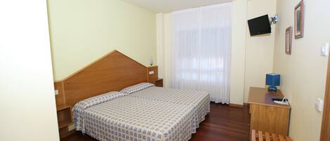 A bedroom with a wooden bed, a desk with a lamp, and a TV mounted on the wall.