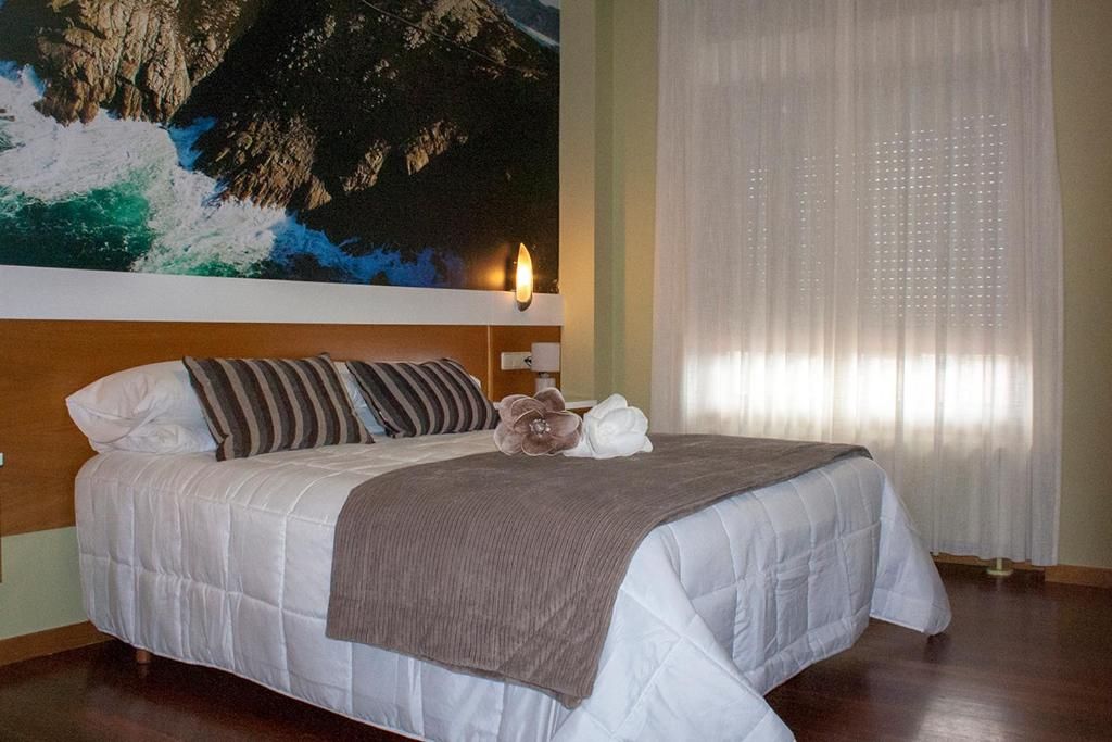 Habitación de hotel con una cama grande, un cuadro en la pared, una mesita de noche con lámpara y cortinas de gasa.