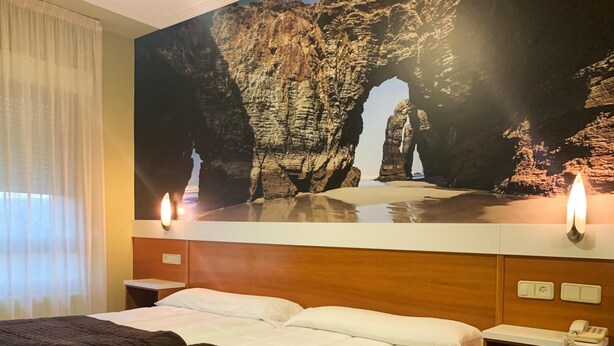 Ein Hotelzimmer mit Bett, Nachttisch, fest montiertem Telefon und einem großen Gemälde mit Felsformationen über dem Bett.